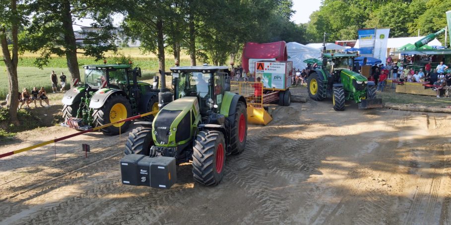 Drei Traktoren auf einem sandigen Weg, umgeben von einem festlichen Ambiente und Bäumen.